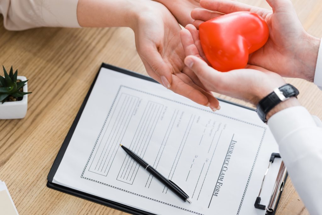 partial view of doctor and patient holding red heart in hands, medical insurance concept